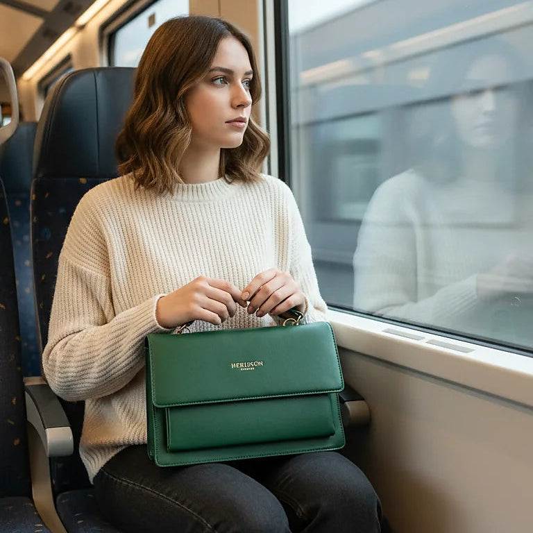Woman sitting on a train holding a green bag, looking out the window.