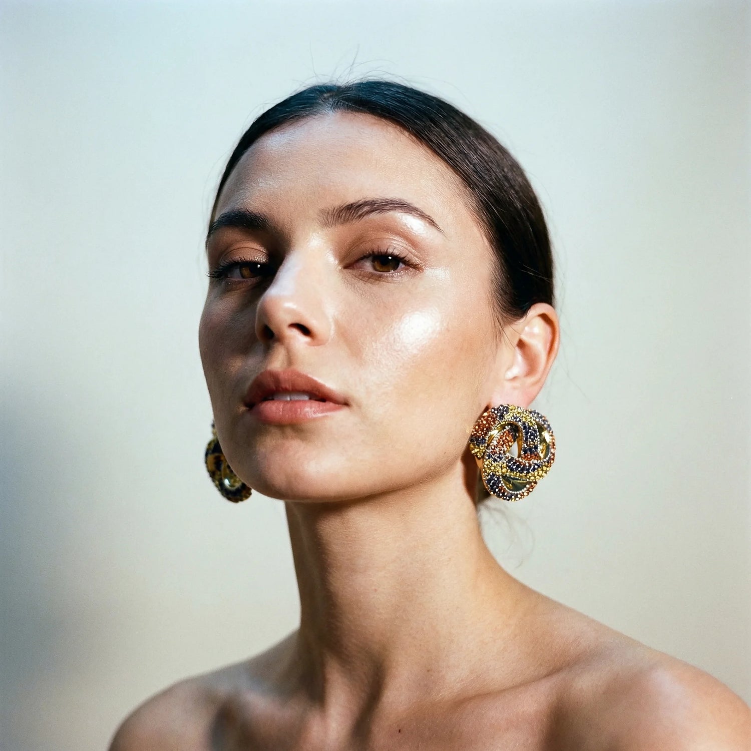 Woman wearing large, ornate earrings against a neutral background