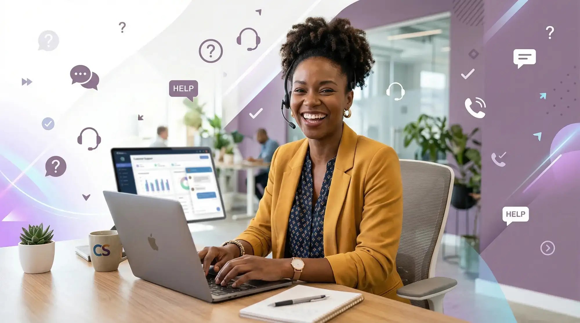 Una donna sorridente con un blazer giallo senape siede alla sua scrivania, digitando su un laptop argento con il logo della mela.