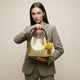 Gold textured leather bucket bag with braided handle and yellow fuzzy character charm