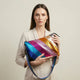 A vibrant, rainbow-striped crossbody bag with a shimmering metallic finish and an adjustable strap.